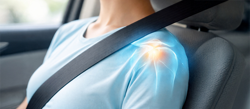 Close-up of a person in a car clutching their shoulder in pain from a seatbelt injury following an auto accident